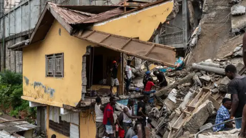     Prince Samura/EPA Gambar rumah yang hancur saat tim penyelamat dan warga menggali untuk menyelamatkan nyawa mereka di reruntuhan bangunan yang runtuh di Freetown, Sierra Leone - Senin 16 September 2024.