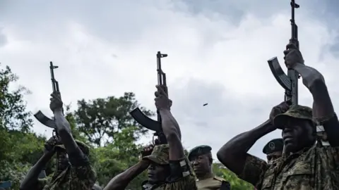 Badru Katumba/AFP Gambar tentara Uganda memberi hormat senjata kepada pelari maraton Uganda Rebecca Cheptegei di Distrik Bukwo, Uganda - Sabtu 14 September 2024.