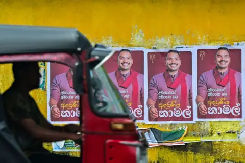 Getty Images Sebuah ojek berwarna merah melewati tembok kuning dengan poster pria berjilbab merah.