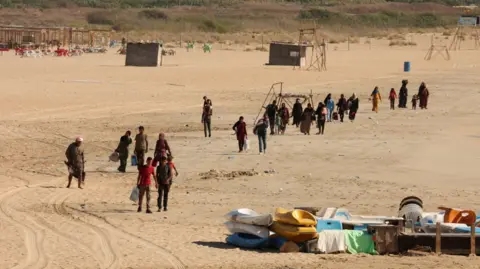 Reuters Orang-orang membawa barang-barang mereka melintasi pantai ketika mereka meninggalkan Tirus - salah satu kota di Lebanon selatan yang terkena serangan pada hari Senin