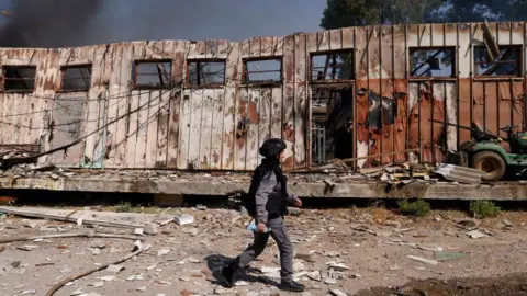 Getty Images Seorang anggota pasukan keamanan Israel berjalan melewati sebuah bangunan yang rusak di lokasi serangan roket di Kiryat Shmona, Israel utara, pada 24 September.