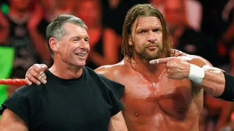 Getty Images Vince McMahon dan Triple, berdiri di atas ring, Triple H menunjuk ke arah Vince. Ada kerumunan di belakang mereka.