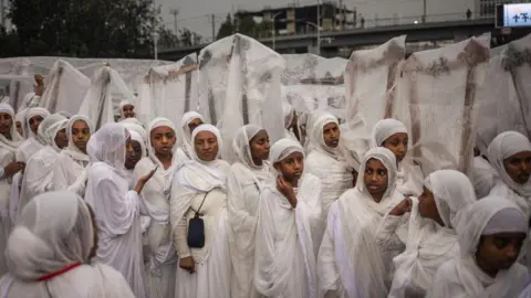 Michel Spotari / AFP Pemain Begena (alat musik kecapi kotak sepuluh senar tradisional) menutupi instrumen mereka dari hujan selama perayaan untuk menandai hari raya meskel Ortodoks Ethiopia pada 26 September 2024 di Addis Ababa.