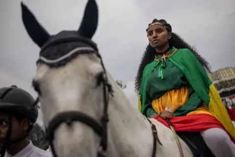 Michel Spotari/AFP Seorang wanita mengenakan pakaian kerajaan berparade di atas kuda saat perayaan hari raya Meskel Ortodoks Ethiopia di Addis Ababa pada 26 September 2024.