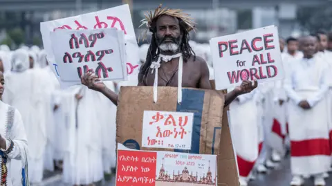     Emmanuel Sileshi / AFP Seorang pria berpose untuk foto sambil memegang plakat saat perayaan hari raya Meskel Ortodoks Ethiopia di Addis Ababa pada 26 September 2024.