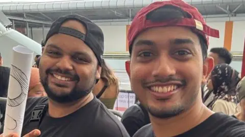 Dwayne Dias Dwayne Dias (kiri) dan temannya berpose untuk foto di tempat konser di Singapura tempat mereka menonton Coldplay tampil live