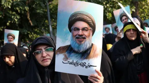 Getty Images Wanita Iran memegang foto pemimpin Hizbullah Hassan Nasrallah, yang tewas dalam serangan udara Israel di pinggiran selatan Beirut pada 27 September.