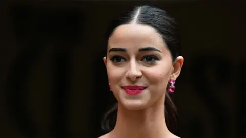 Getty Images Tampilan jarak dekat dari Ananya Pandey - seorang aktris wanita yang mengenakan anting-anting berwarna merah muda tua dan tersenyum. Latar belakangnya berwarna hitam.