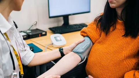 Getty Images Seorang dokter umum yang mengukur tekanan darah seorang wanita di ruang praktik dokter