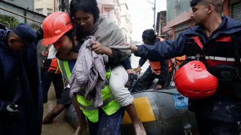 Reuters Seorang polisi membawa seorang wanita yang terluka dari rakit tiup setelah diselamatkan dari daerah banjir di tepi Sungai Bagmati yang meluap di Kathmandu, Nepal.