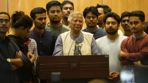 Getty Images DHAKA, BANGLADESH - 8 AGUSTUS: Peraih Nobel Muhammad Yunus (tengah) berbicara saat konferensi pers setelah kedatangannya di Bandara Internasional Hazrat Shahjalal pada 8 Agustus 2024 di Dhaka, Bangladesh. Peraih Hadiah Nobel Perdamaian Muhammad Yunus kembali ke Bangladesh pada 8 Agustus untuk memimpin pemerintahan sementara setelah pemberontakan yang dipimpin mahasiswa mengakhiri 15 tahun pemerintahan Sheikh Hasina. (Foto oleh Sultan Mahmood Mukut/Druk/Getty Images)