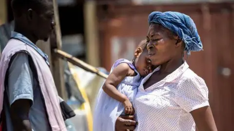 Getty Seorang wanita pada 27 Agustus 2024 di Ecole Nationale Joseph C. di Port-au-Prince, Haiti. Seorang anak digendong melintasi halaman sekolah di kamp pengungsian Bernard DeFreres. 