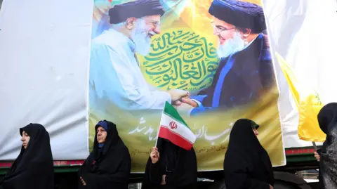 EPA Wanita Iran berdiri di depan poster Pemimpin Tertinggi Iran Ayatollah Ali Khamenei (kiri) dan mendiang pemimpin Hizbullah Hassan Nasrallah (kanan) selama unjuk rasa anti-Israel di Teheran, Iran (27 September 2024).