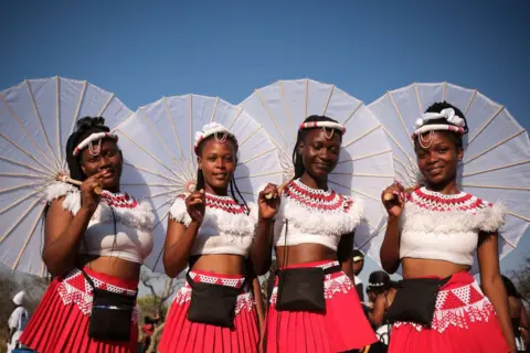 MKHULULI SIBANDS / GETTY IMAGES Remaja putri mengenakan gaun merah putih yang serasi dan membawa payung yang serasi.