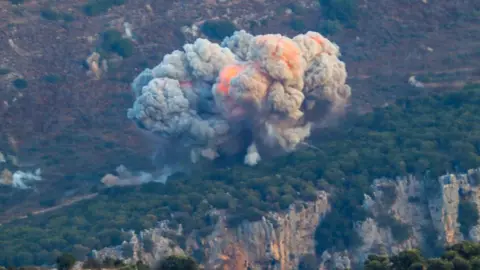 Getty Images Asap mengepul dari lokasi serangan udara Israel di Marjayon, dekat perbatasan Lebanon-Israel, pada 23 September.