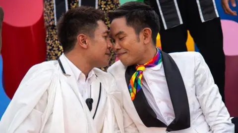 Getty Images Pasangan gay - dua pria - duduk berdekatan dengan kepala saling bersentuhan dalam upacara yang diselenggarakan oleh pemerintah Thailand untuk menandai disahkannya undang-undang kesetaraan pernikahan pada bulan Juni.

