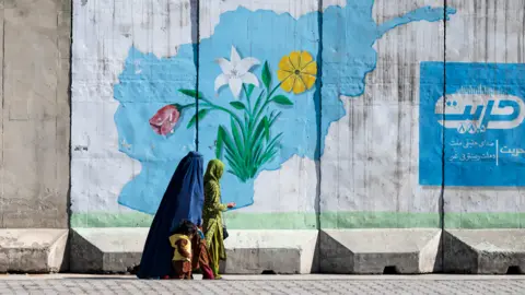 Getty Images Seorang wanita Afghanistan yang mengenakan burqa berjalan melewati mural dinding dengan peta Afghanistan di Kabul pada 1 Februari 2024. (Foto oleh Vakil Kohsar/AFP) (Foto oleh Vakil Kohsar/AFP via Getty Images)