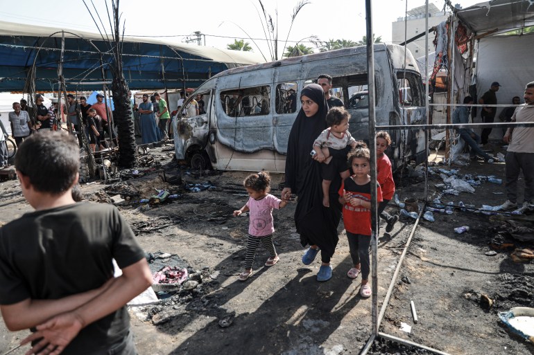 Madi berjalan bersama anak-anaknya melewati kehancuran yang disebabkan oleh pemboman Israel terhadap kamp pengungsi di halaman Rumah Sakit Syahid Al-Aqsa