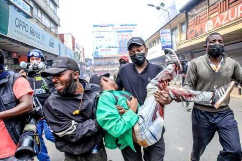 Getty Images Seorang pengunjuk rasa muda yang marah membantu seorang kawannya yang ditembak mati dalam demonstrasi menentang pembunuhan polisi terhadap orang-orang yang memprotes rancangan undang-undang ekonomi Kenya di Nairobi pada 2 Juli. 