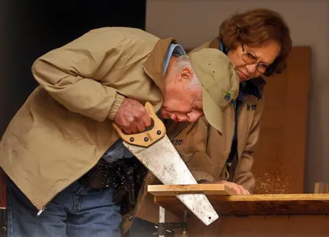 Getty Images Carter dan Rosalyn Carter memotong sepotong kayu dengan gergaji