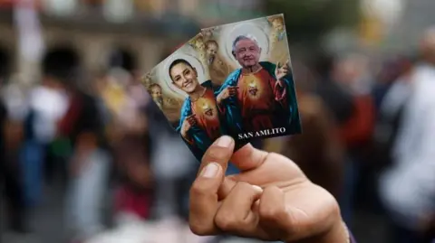 EPA Seorang pria memegang dua kartu Presiden Meksiko Claudia Sheinbaum (kiri) dan mantan Presiden Meksiko Andres Manuel Lopez Obrador, di Jocalo, Meksiko City, 01 Oktober 2024.