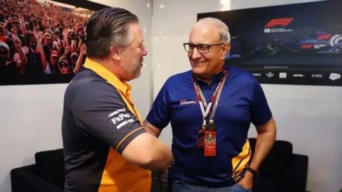 Getty Images Subramanian Eswaran berjabat tangan dengan CEO McLaren Jack Brown di depan televisi yang menayangkan Formula 1