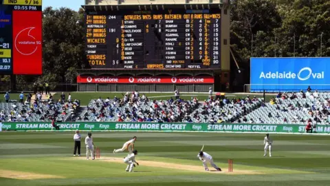 AFP Pat Cummins dari Australia (3/kiri) mengalahkan pemain India Mohammed Shami (2/kanan) dengan penjaga saat India tersingkir untuk 36 pada hari ketiga Tes kriket pertama antara Australia dan India di Adelaide pada 19 Desember. 2020. (