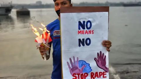 Getty Images KOLKATA, INDIA - 30/11/2019: Seorang pengunjuk rasa memegang plakat bertuliskan 'Hentikan pemerkosaan' dan menyalakan lilin selama protes untuk keadilan dan menentang kasus pemerkosaan berkelompok terhadap Priyanka Reddy. Priyanka Reddy, seorang veteran perempuan (26 tahun) dari Hyderabad, India, diperkosa beramai-ramai dan dibakar hidup-hidup pada tanggal 28 November oleh empat pengemudi truk di jalan raya, menurut polisi. Menurut kabar terbaru, Hakim kota Shadnagar di Telangana mengirim keempat terdakwa ke tahanan yudisial selama 14 hari. (Foto oleh Avishek Das/SOPA Images/Lightrocket via Getty Images)