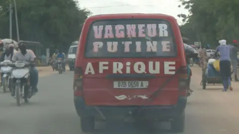 Getty Images Gambar yang diambil melalui jendela kendaraan menunjukkan sebuah minibus dengan huruf di jendela belakang mewakili Presiden Rusia Vladimir Putin dan kelompok paramiliter Rusia Wagner, N'Djamena - 3 September 2024.