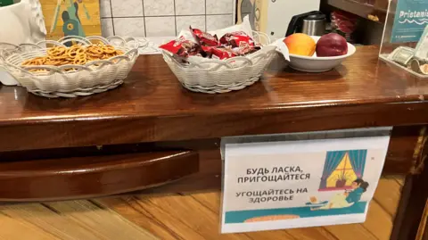 Sebuah tanda dalam bahasa Ukraina dan Rusia di Pristaniste Cafe mengundang warga untuk mengambil sendiri makanan ringan