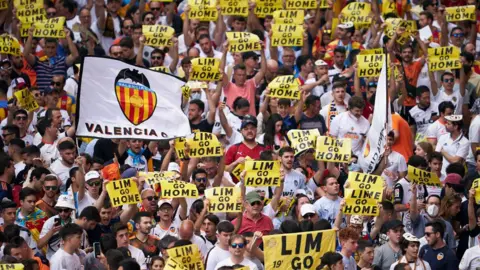 Getty Images Ratusan orang, banyak yang memegang tanda 'LIM GO HOME', melakukan protes sebelum pertandingan di Valencia