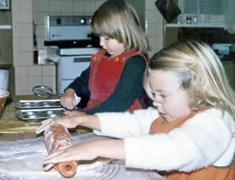 Foto masa kecil Kylie Minogue memperlihatkan Kylie Minogue menggelar kue di dapur keluarga