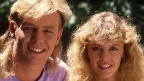 Getty Images Jason Donovan dan Kylie Minogue berpose di lokasi syuting sinetron Australia Neighbors pada tahun 1987