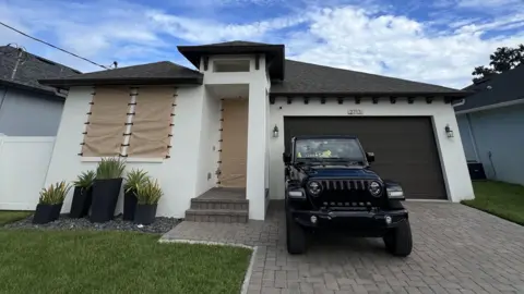 Rumah Perkins kecil dengan jendela yang disembunyikan sementara oleh penutup Kevlar dan kendaraan diparkir di luar 