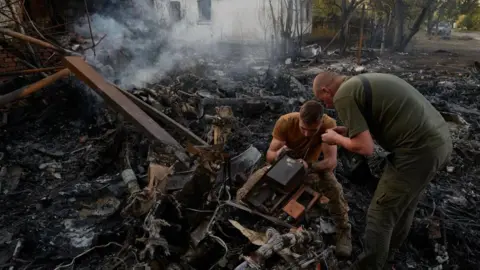 Pierre Crom/Getty Images Tentara Ukraina memeriksa puing-puing pesawat Rusia yang jatuh, kemungkinan Sukhoi S-70 