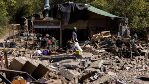 Reuters 8 Oktober 2024, Seorang warga berjalan melewati puing-puing setelah lewatnya Badai Helene di Marshall, North Carolina