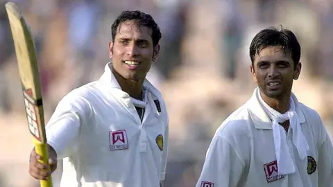 Getty Images Pemukul India Venkat Sai Laxman (Kiri) mengarahkan tongkat pemukulnya ke arah penonton yang bersorak saat rekan setimnya Rahul Dravid melihat saat dia berjalan kembali ke paviliun pada hari keempat pertandingan Tes kedua antara India dan Australia di Taman Eden di Kalkuta. 14 Maret 2001. 