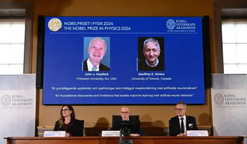 Getty Images Layar menunjukkan peraih Hadiah Nobel Fisika tahun 2024, fisikawan AS John J Hopfield (kiri atas) dan ilmuwan komputer dan psikolog kognitif Kanada-Inggris Geoffrey E Hinton (kiri bawah) ketua Komite Nobel Fisika Ellen Moons, 8 Oktober , Pengumuman tersebut disampaikan oleh Hans Elegren, Sekretaris Jenderal Royal Swedish Academy of Sciences, dan Anders Irback, anggota Komite Nobel Fisika, di Royal Swedish Academy of Sciences di Stockholm, Swedia, 2024. John Hopfield dari Amerika dan Geoffrey Inggris-Kanada. Hinton memenangkan Hadiah Nobel Fisika pada 8 Oktober 2024 atas karya pionirnya dalam pengembangan kecerdasan buatan.