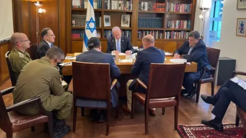 Kantor Perdana Menteri Israel PM Benjamin Netanyahu, berfoto saat melakukan panggilan telepon dengan Presiden Biden. Dia duduk bersama tujuh asistennya di meja kayu, dengan bendera Israel terlihat di belakangnya.