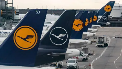 Getty Images Sayap ekor delapan pesawat Lufthansa diparkir di gerbang Bandara Frankfurt.