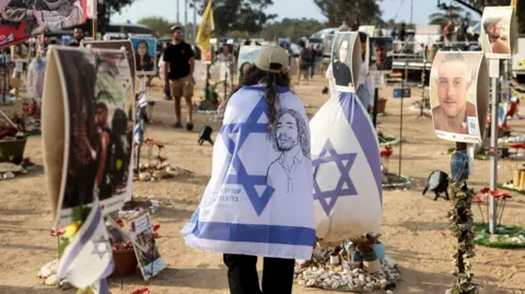 Seorang wanita yang mengenakan topi baseball berwarna krem ​​​​dan membawa bendera Israel lewat saat orang-orang mengunjungi lokasi festival Nuh.