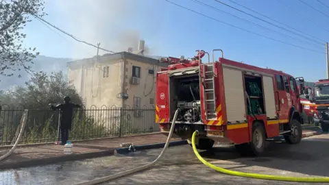 Petugas pemadam kebakaran BBC memadamkan api di sebuah bangunan tempat tinggal yang terkena roket Hizbullah di Kiryat Shmona, Israel utara (9 Oktober 2024).