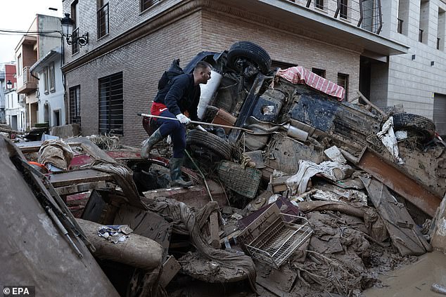 Seorang pria berjalan melewati puing-puing untuk mengakses jalan yang tertutup lumpur di kota Paiporta, Valencia, Spanyol, 7 November 2024 yang dilanda banjir