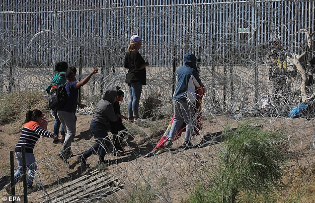 Para migran menunggu di antara kawat berduri dekat tembok perbatasan AS ketika mereka mencoba memasuki El Paso, Texas, pada 26 Mei